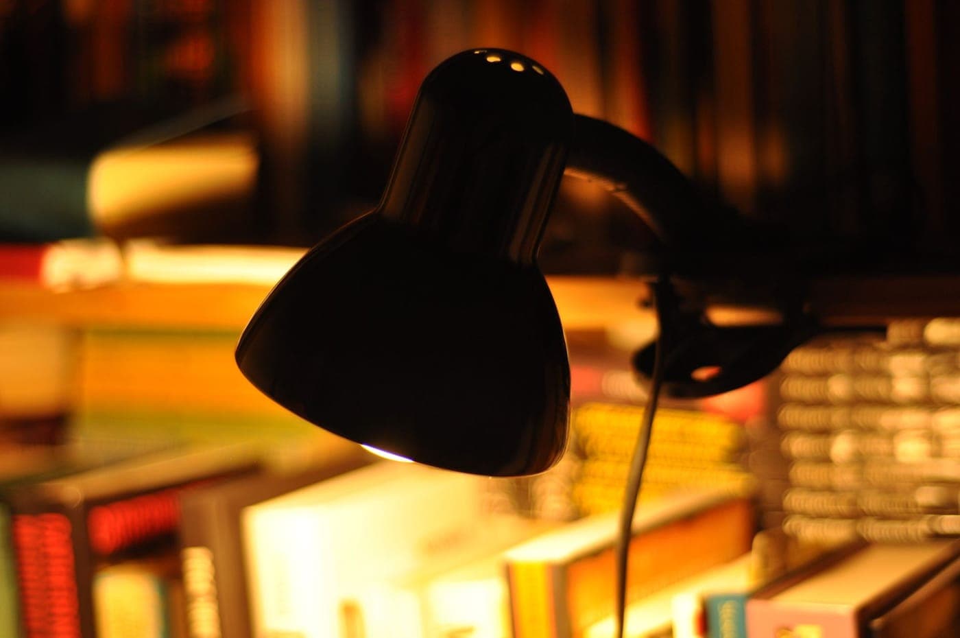 A warm desk lamp lighting a corner with books in the evening