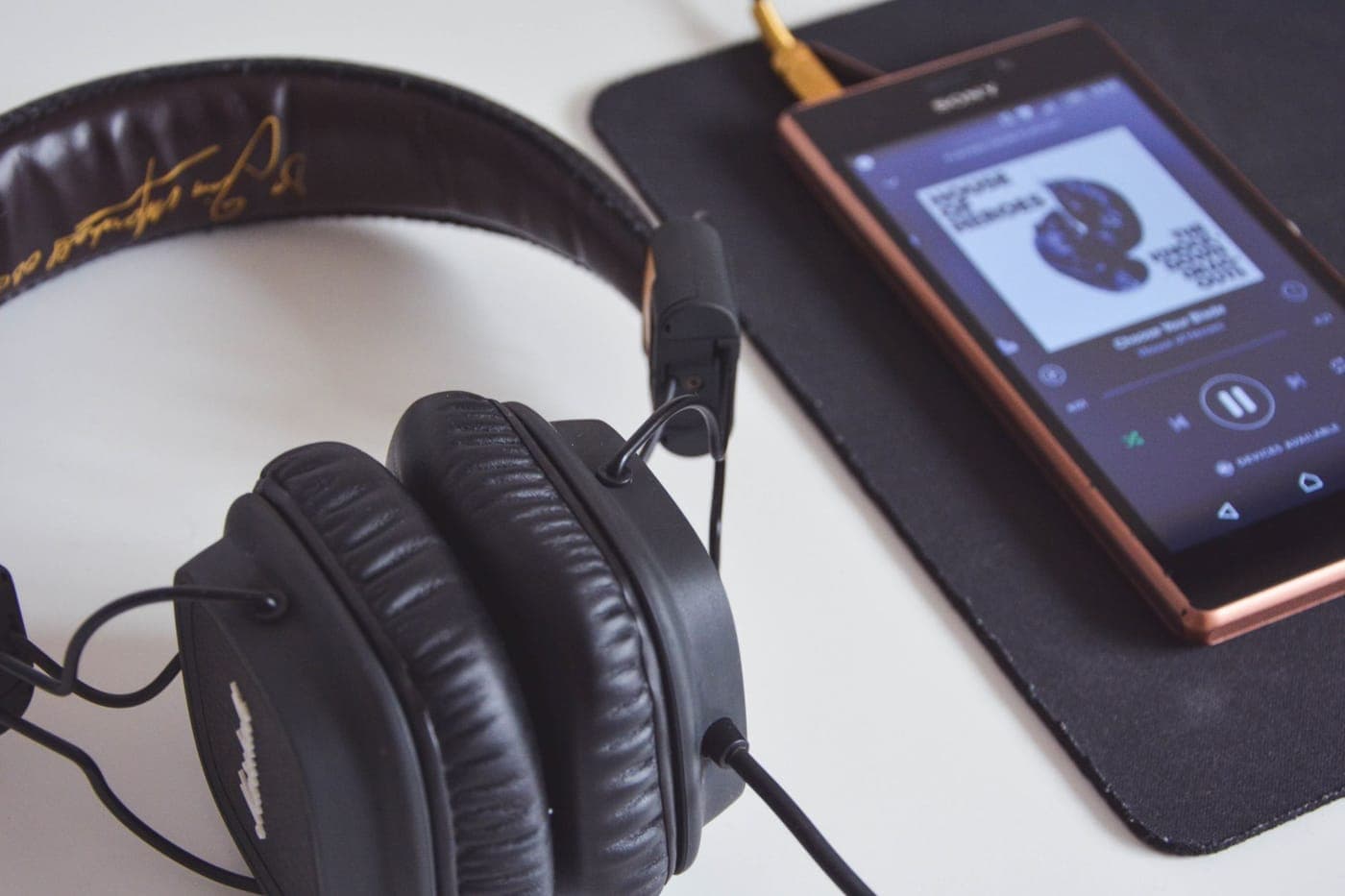 Headphones and a phone on a desk beside a notebook